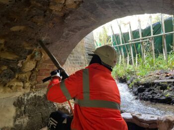 man wearing high visibility clothing and helmet using tool to make assessments underground