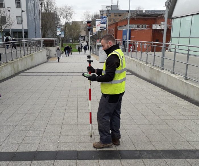 man in high visibility jacket standing on pathway using equipment to conduct a topographic survey