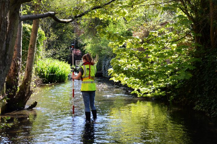 woman standing in lake using a piece of equipment to conduct a topographic survey
